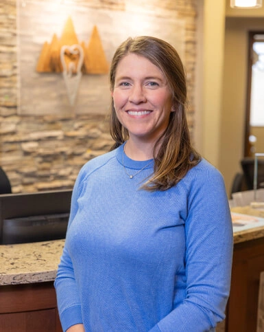 Woman in blue shirt smiling at dental office reception area with stone accent wall.