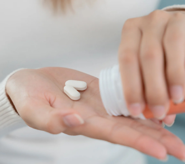 Person holding white medication pills in palm of hand against blurred background.