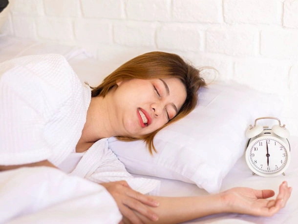 Woman sleeping peacefully in bed holding alarm clock, depicting rest and sleep health.