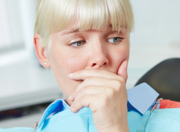 Young child in blue shirt looking worried, hand near mouth, suggesting dental concern or anxiety.