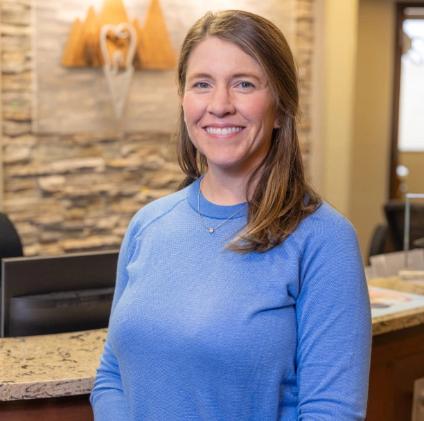 Woman in blue shirt smiling at camera in modern dental office reception area.