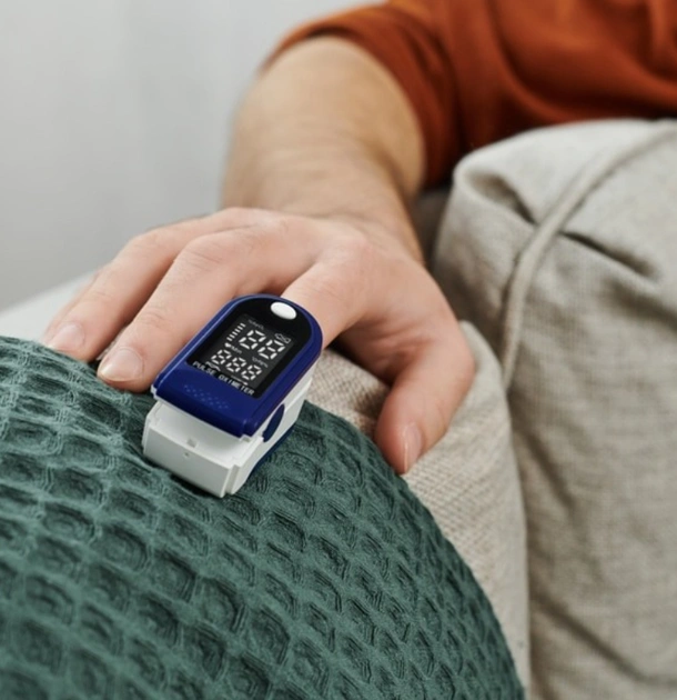 Person wearing smartwatch with blue face and white band on wrist, seated indoors.