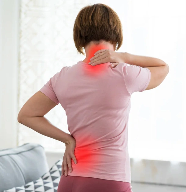 Person holding neck and lower back in pain, wearing pink shirt indoors.