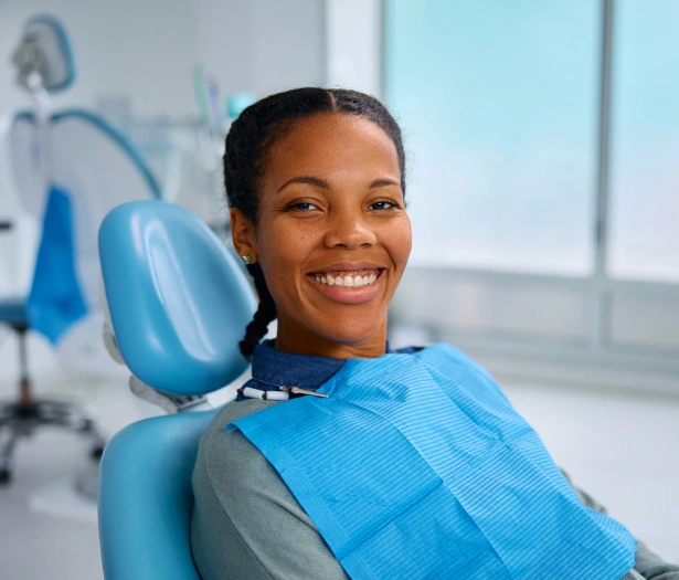 Smiling woman in dental chair at modern dental office with equipment visible in background.