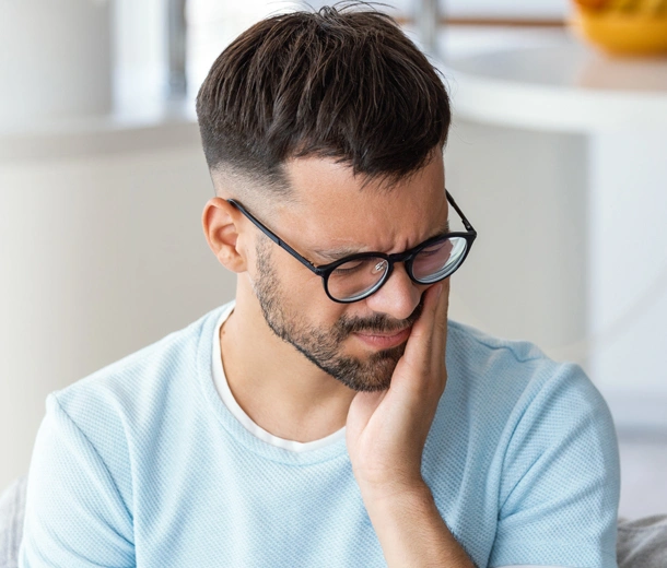 Man wearing glasses in light blue shirt, thoughtful expression, hand to face, indoor office setting.