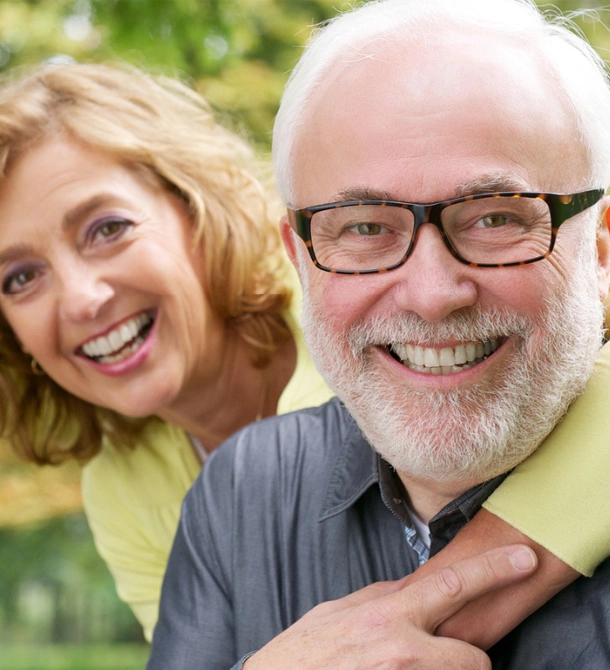 Two smiling adults posing together outdoors with green blurred background.