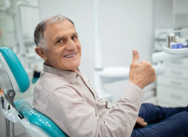 Smiling male patient giving thumbs up in dental chair at periodontal office