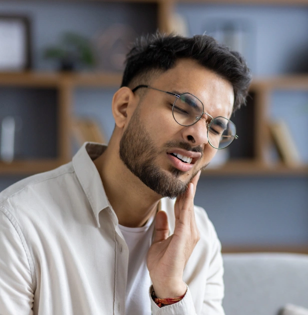 Male dentist wearing glasses and white coat smiling in modern office setting.