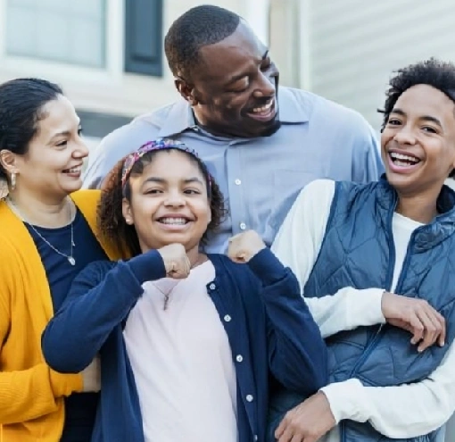 Happy family of four smiling together outdoors in front of a house.